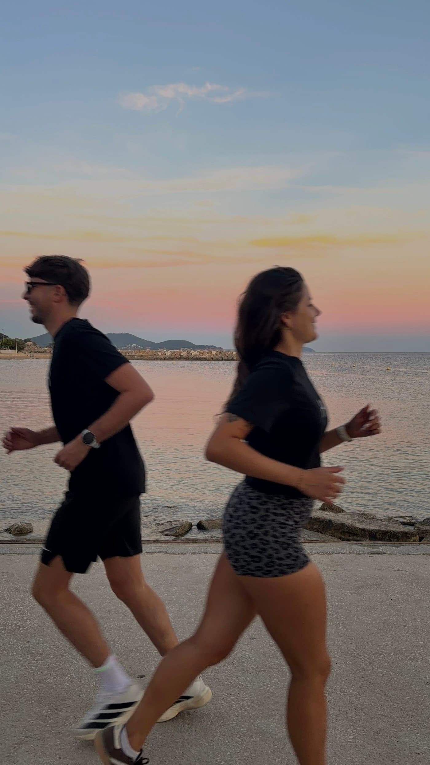 Deux membres du club courant côte à côte au bord de mer au coucher du soleil, en tee-shirts noirs