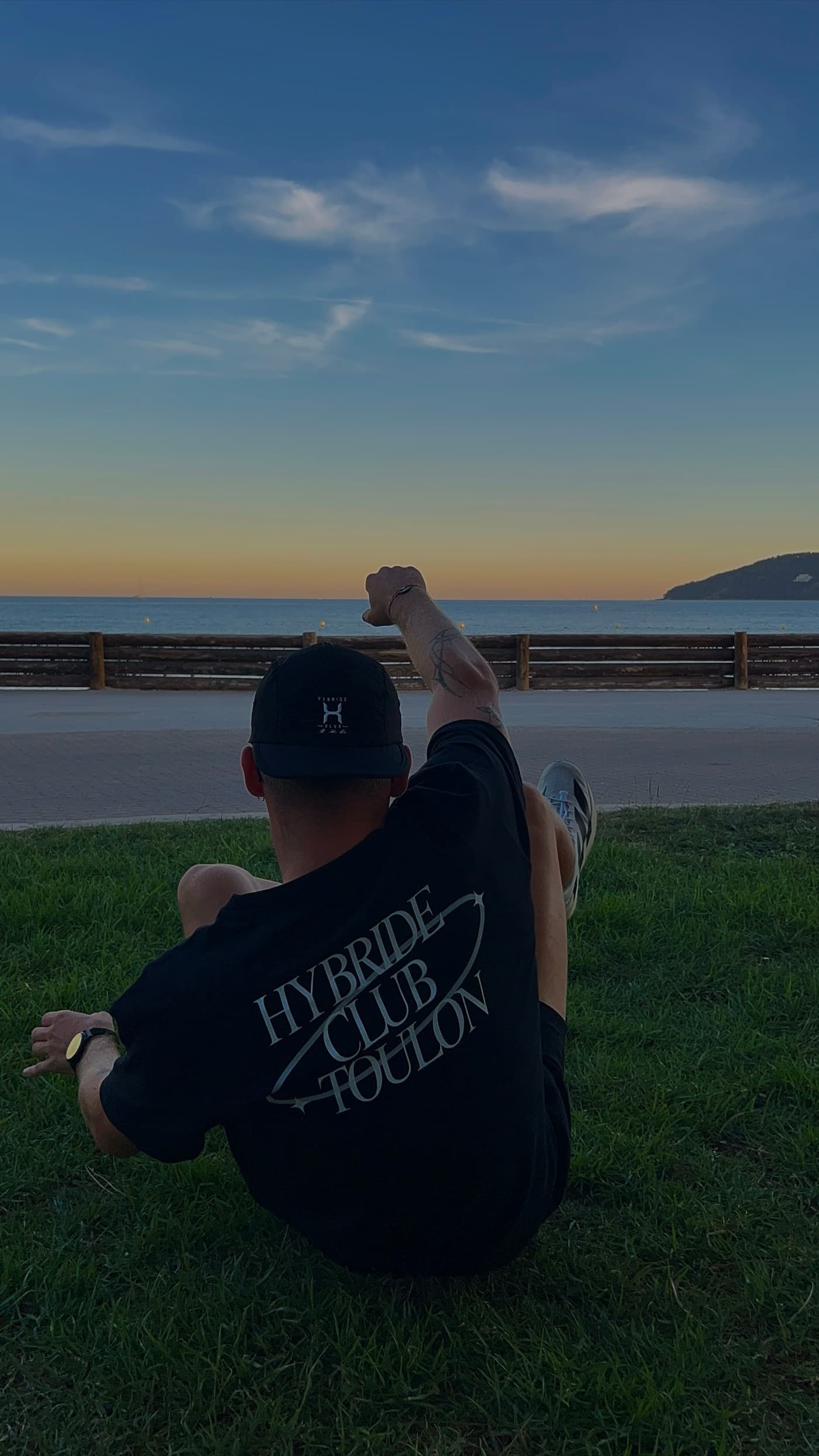 Un membre du club assis de dos dans l’herbe, tee-shirt noir floqué Hybride Club Toulon