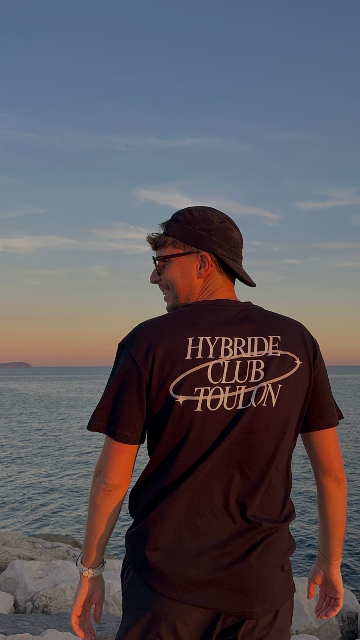 Un membre du club de dos face à la mer, grand floquage Hybride Club Toulon sur le tee-shirt noir