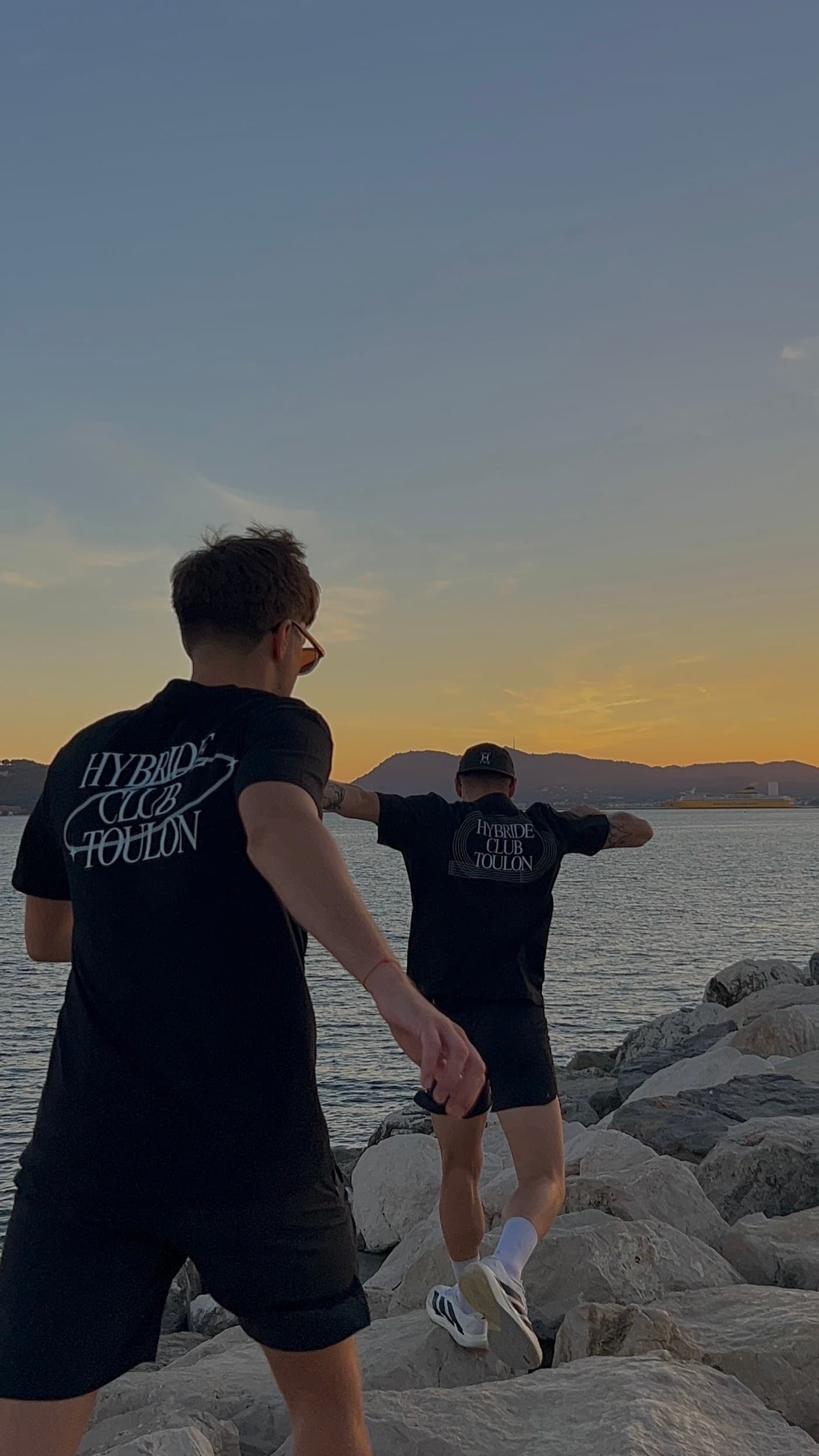 Deux membres du club sur les rochers au coucher du soleil, tee-shirts noirs floqués dans le dos