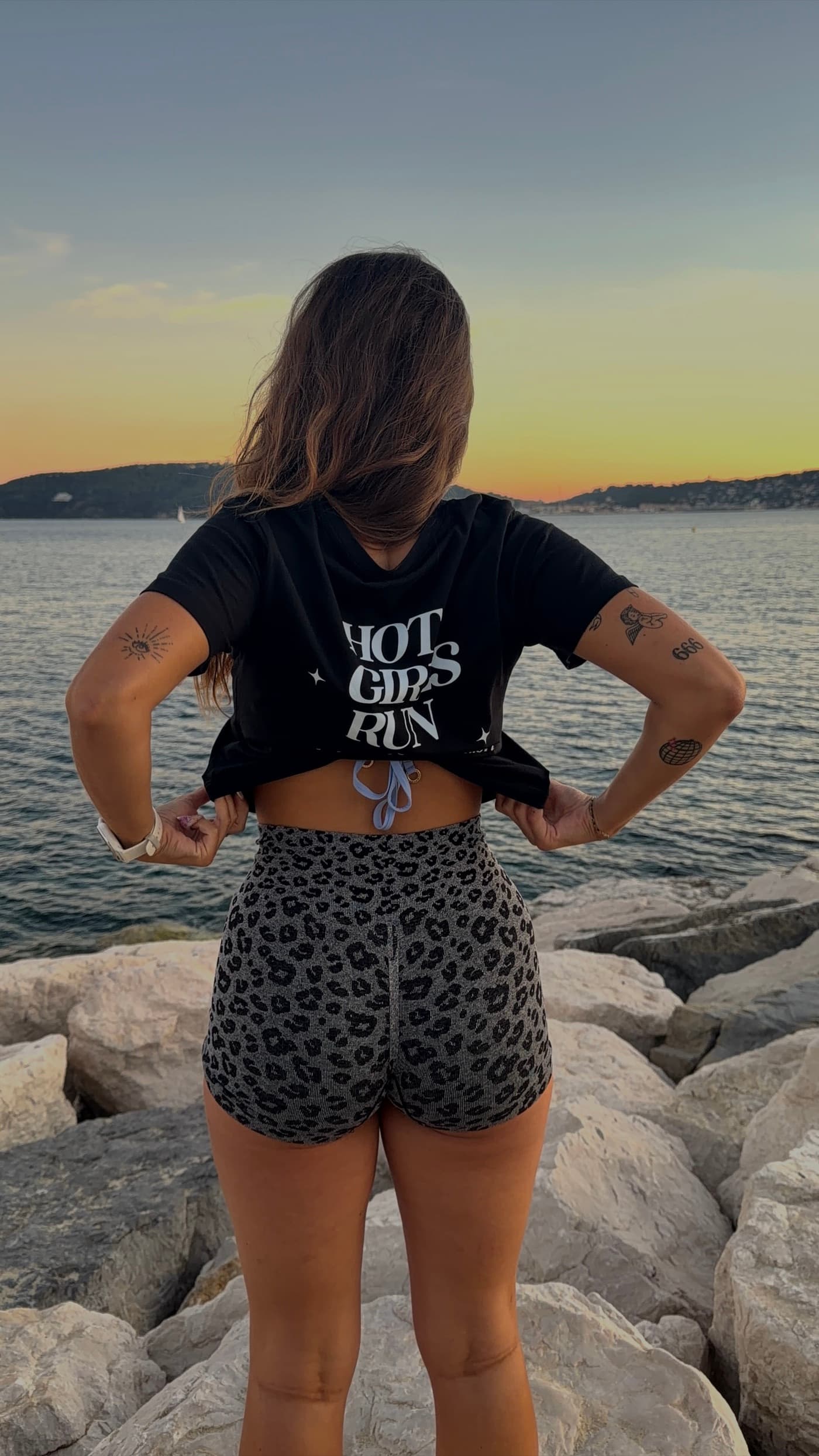 Une membre du club de dos sur les rochers, tee-shirt noir floqué Hot Girls Run