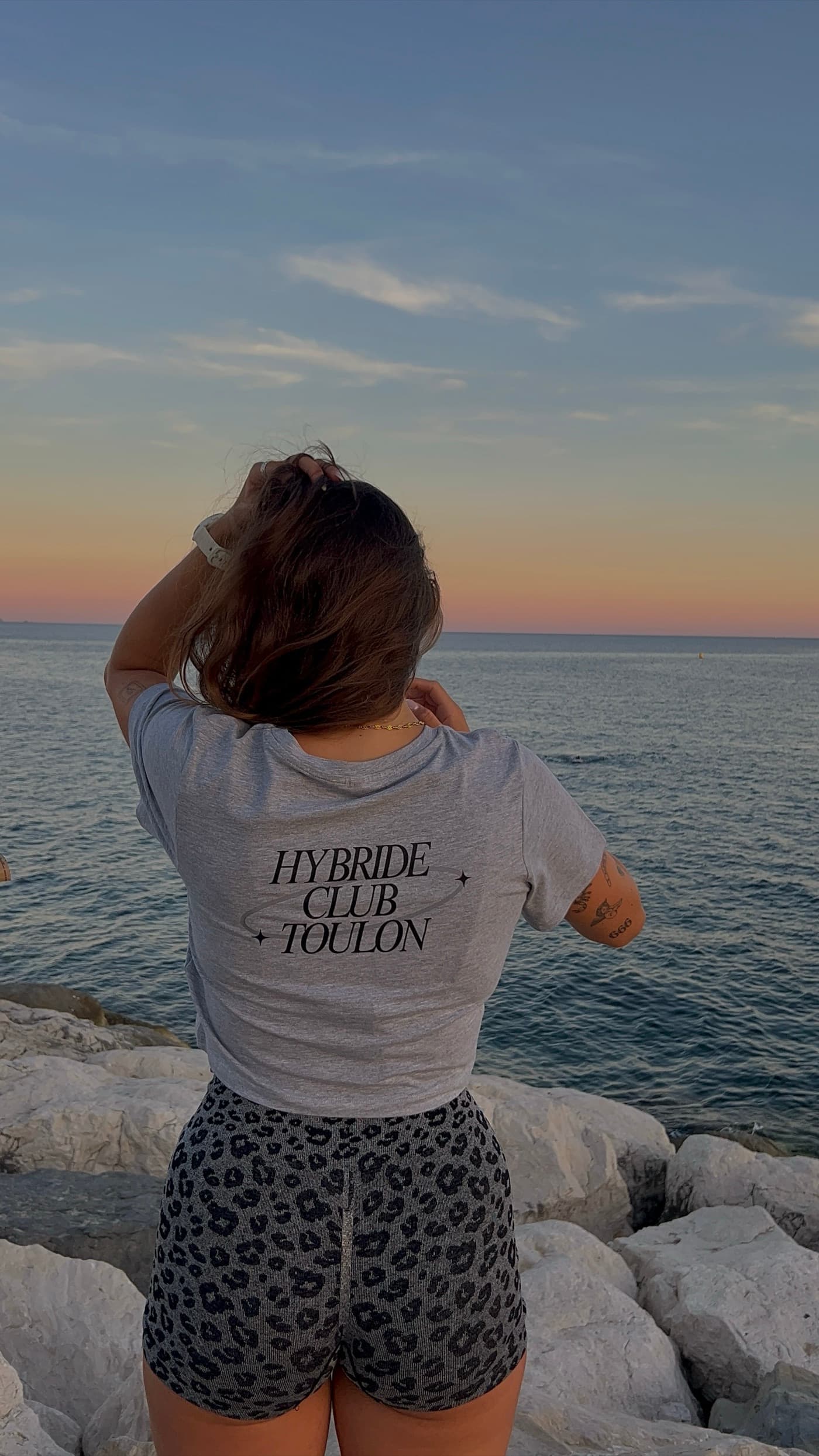 Une membre du club de dos sur les rochers, tee-shirt crème floqué Hybride Club Toulon