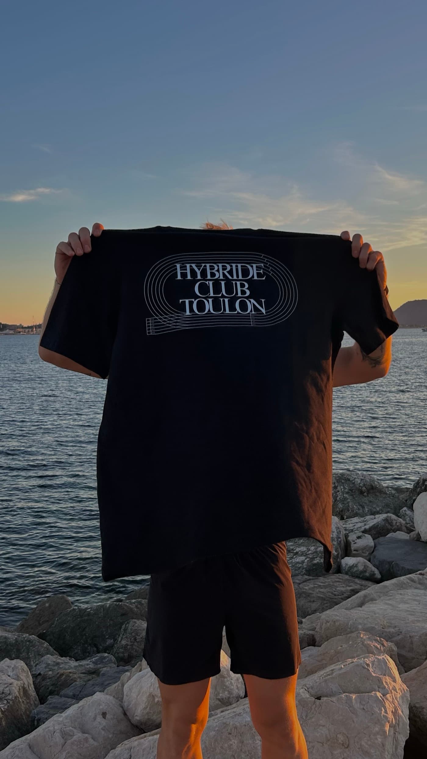 Un tee-shirt noir du club déployé à bout de bras sur les rochers, au coucher du soleil