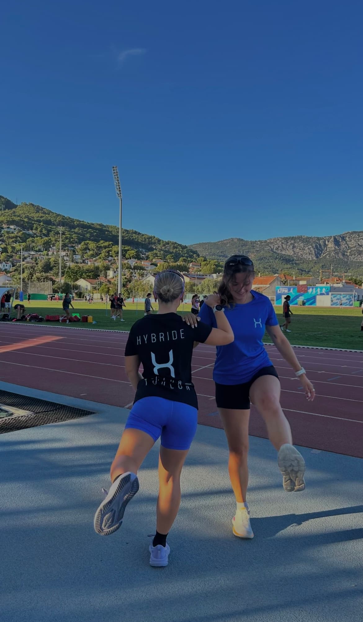 Deux membres du club de dos sur la piste, floquage Hybride dans le dos, collines à l’horizon