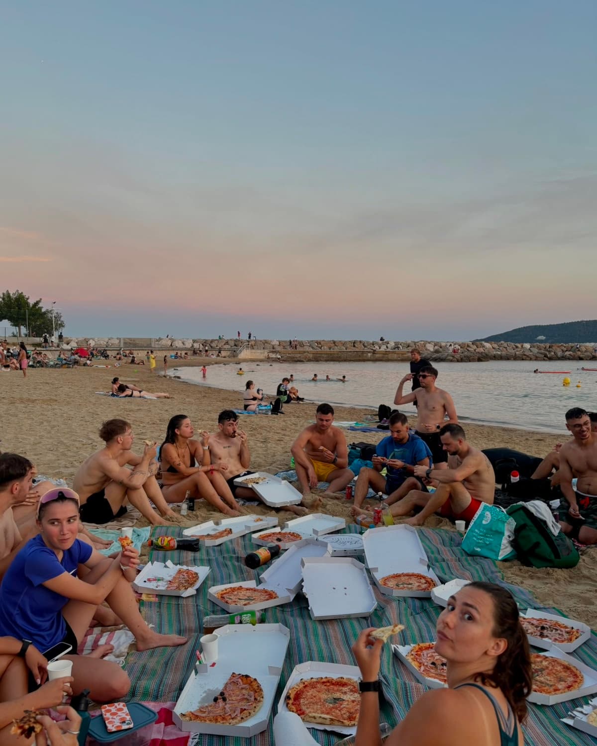 Le groupe du club partageant des pizzas sur la plage au coucher du soleil
