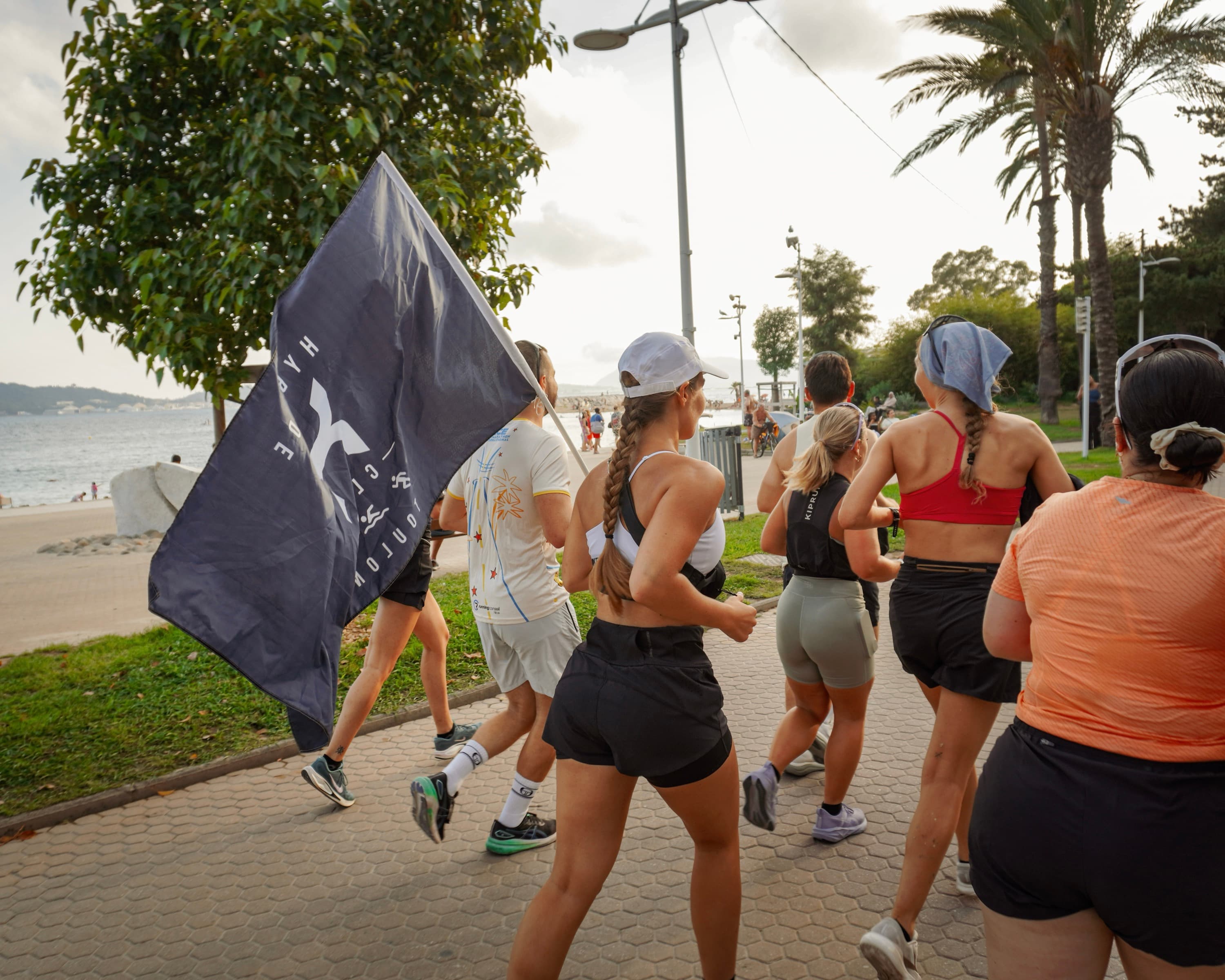 Groupe de coureurs du club Hybride Toulon portant le drapeau du club le long du bord de mer